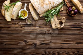 Delicious homemade italian ciabatta bread with olive oil and olives on wooden rustic background, above view