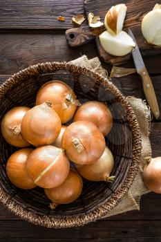 Fresh onion in basket on wooden table, top view