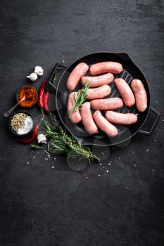 Fresh raw sausages on a cast-iron grill pan on a black background, top view