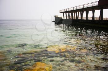 Old concrete, stone pier and the bridge in the sea. Beautiful dark sea with rich color and clear water and stones