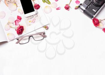 The composition of red roses, petals, magazine, phone, camera on a white background. Soft focus. View from above. Designer working space concept, creative person