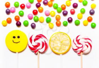 Lollipops, candy smile on, are scattered around the colorful jelly beans on a white background.  Top view, flat