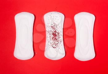 Three sanitary pads on a coral red background. The concept of critical days, menstruation, women's periodic cycle.