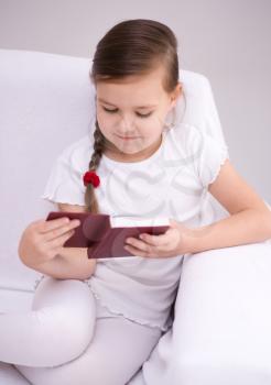 Cute little girl is reading book while sitting on a couch, indoor shoot