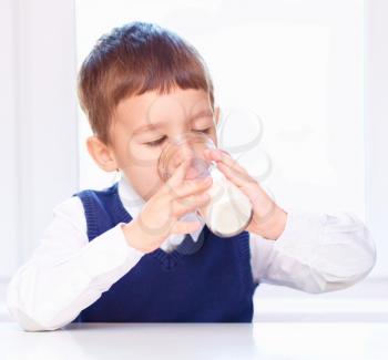 Cute little boy is dipping his tongue in the glass of milk