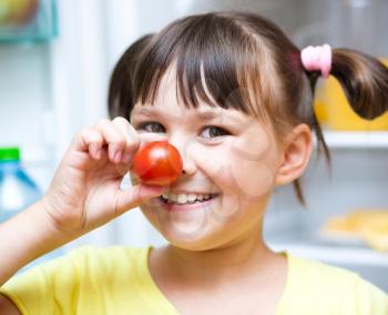 Happy girl eating tomatoes standing near refrigerator with fruits and vegetables