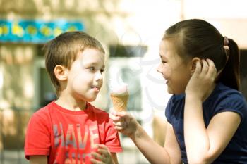 Girl is feeding his little brother with ice-cream. Outdoor