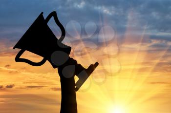 Champion and winning concept. Silhouette of a hand holding a championship trophy against the sky