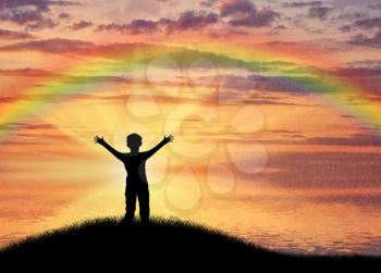 Happy child standing beside sea on hill sunset sky and rainbow. Childhood concept