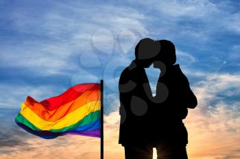 Concept of gay people. Silhouette happy gay kissing against the evening sky and a rainbow flag