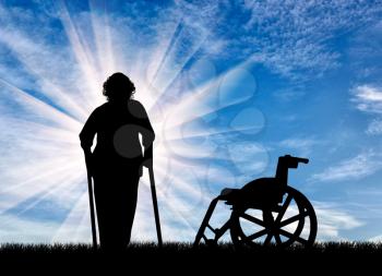 Silhouette of an elderly woman with crutches on background of wheelchair outdoors. Concept of disability and old age