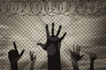 Concept of emotions and feelings. Silhouette refugees hands near the border fence on the sunset background