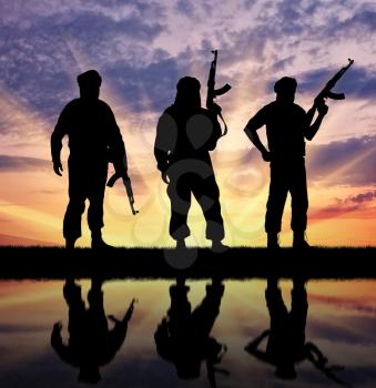 Silhouette of three terrorists with weapons at sunset with reflection in water