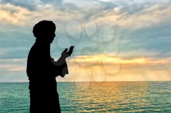 Concept of Islamic culture. Silhouette of man praying on the background of the sea and a beautiful sunset