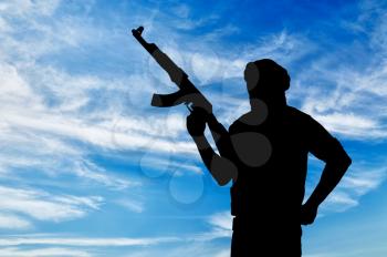 Silhouette of a terrorist with a weapon against a blue sky