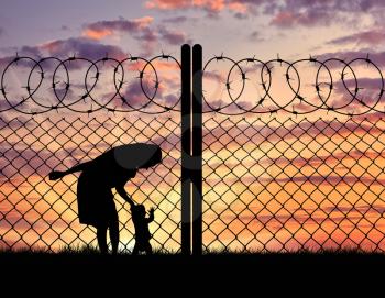 Concept of the refugees. Silhouette mother with child refugees near the fence at sunset