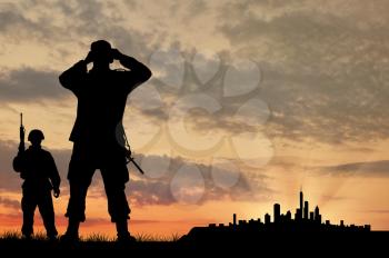 Silhouette of two soldiers with guns looking through binoculars over the city at sunset