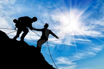 Concept of aid. Silhouette of two climbers help each other