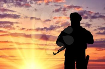 Concept of terrorism. Silhouette of a terrorist with a weapon against a background of a sunset