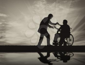 Man helps man in wheelchair to stand up on background sunset. Concept help disabled persons