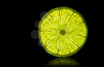 Lime slice backlit isolated on a black background with reflection. design element