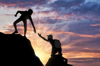Silhouette of a male mountaineer giving a helping hand to his partner. Concept of a climber's help hand