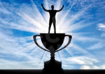 The concept of leadership in business. Silhouette of a happy businessman standing on the trophy against the sky