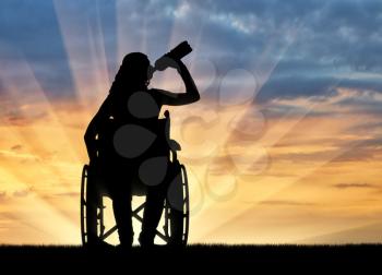 Silhouette of a disabled woman in a wheelchair drinking water from a plastic bottle. Concept of leisure and recreation for disabled people