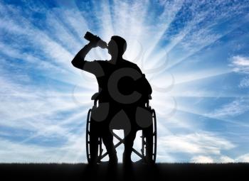 Silhouette of a disabled man in a wheelchair drinking water from a plastic bottle. Concept of leisure and recreation for disabled people
