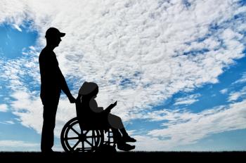 Silhouette of a disabled child girl sitting in a wheelchair reading a book together with a dad. The concept of caring for disabled children