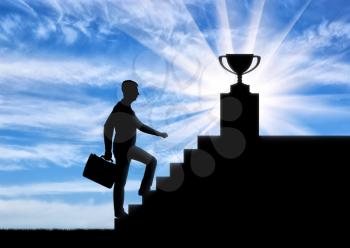 A silhouette of a businessman climbs the stairs to the trophy. Business success concept