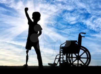 Children with disabilities concept. Happy disabled boy with a prosthetic leg standing near a wheelchair against the sky