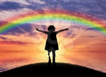 A happy child is a disabled girl with a prosthetic leg in the open air on the background of sea sunset and rainbow. The concept of happy children with prosthetic legs