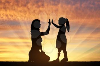 Disabled baby girl with prosthetic legs with her mom outdoors at sunset. The concept of children with prosthetic leg