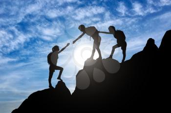 Silhouette of two female mountaineers helping another female mountaineer to overcome the obstacle in the mountains. Conceptual scene of a girl climbers