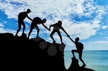 Men climbers help each other in the mountains against the background of the sea. Conceptual scene of male mountaineers work in a team