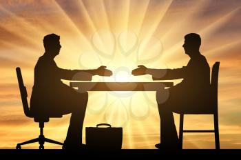 Silhouette of two men sitting at a table and stretching out their hands for a handshake against a sunset. Concept hiring process