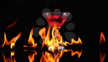 Hot chili pepper in a martini glass with a fire on a black background