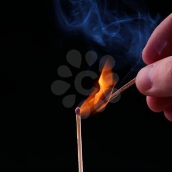 Ignition of a match, with smoke on dark background. Hand holding burning match stick