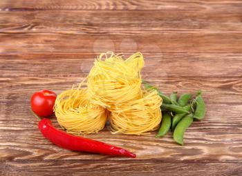 Pasta on the wooden background with tomato, peas and peppers