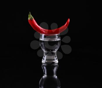 Hot chili pepper in a  shot glass with a fire on a black background