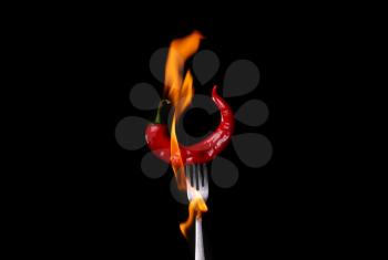 Fork impale to red hot chili on black background.