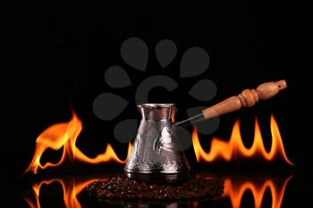 Fired cup of coffee with coffee beans and turk on black background