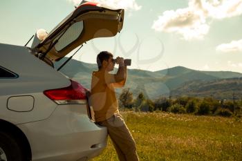 Young Man use of the binocular at forest. Tourist Camping on a car