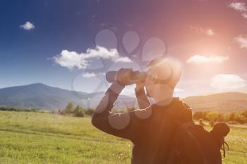 The side profile of Man watching though binoculars. Beautiful mountains landscape with clouds and with tourist binoculars.