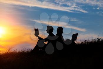 silhouette of a men with laptop and a book on sunset or sunrise background. The idea of the contradictions of the old and new values. The concept of old and modern