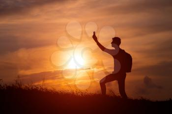 Silhouette of tourist man spread hand on top of a mountain enjoying sunset. Sport and active life concept. man taking photos of sunset with mobile phone