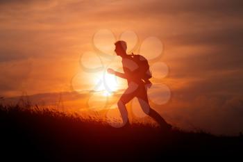Silhouette of tourist man spread hand on top of a mountain enjoying sunset. Sport and active life concept