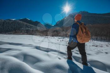 Man with backpack trekking in mountains. Cold weather, snow on hills. Winter hiking. Sun and snow