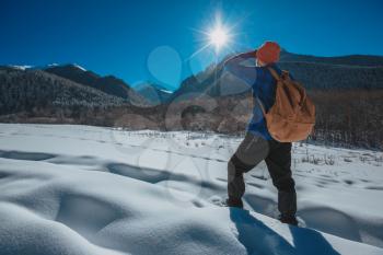 Man with backpack trekking in mountains. Cold weather, snow on hills. Winter hiking. Sun and snow